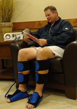 A man sitting on top of a brown couch wearing blue and black pads.