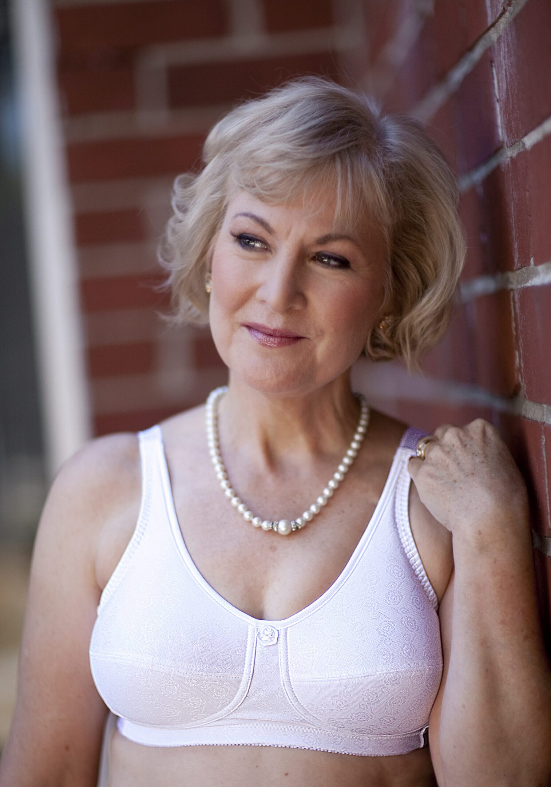 A woman wearing pearls leaning against a brick wall.