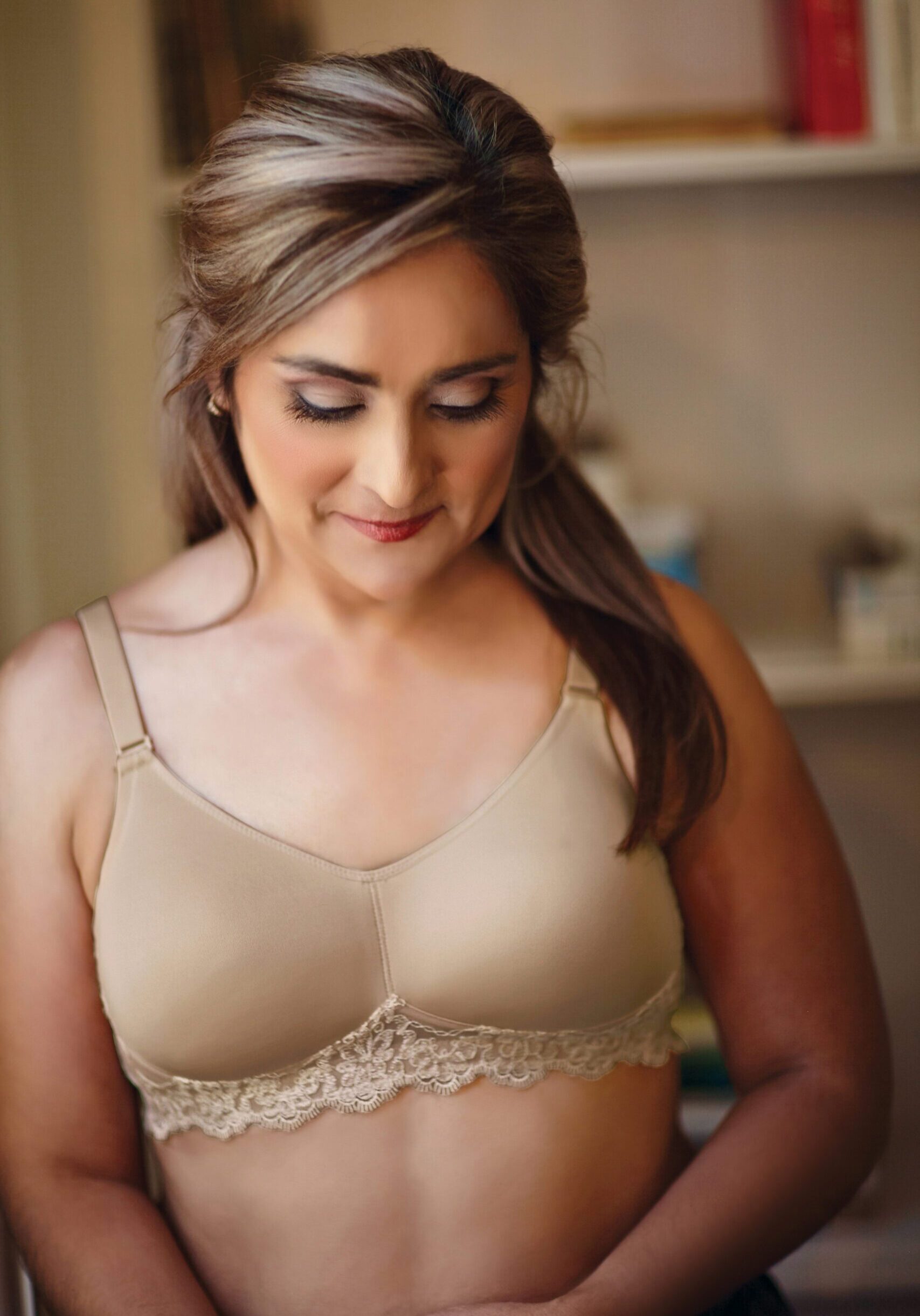 A woman in beige bra looking down at her stomach.