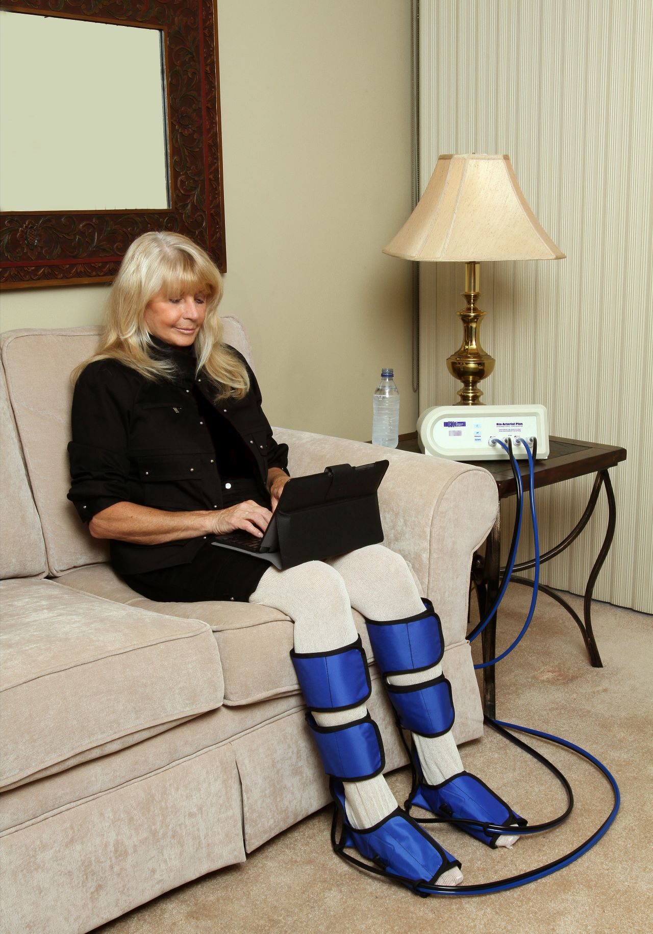 A woman sitting on the couch with her legs wrapped around an electric device.