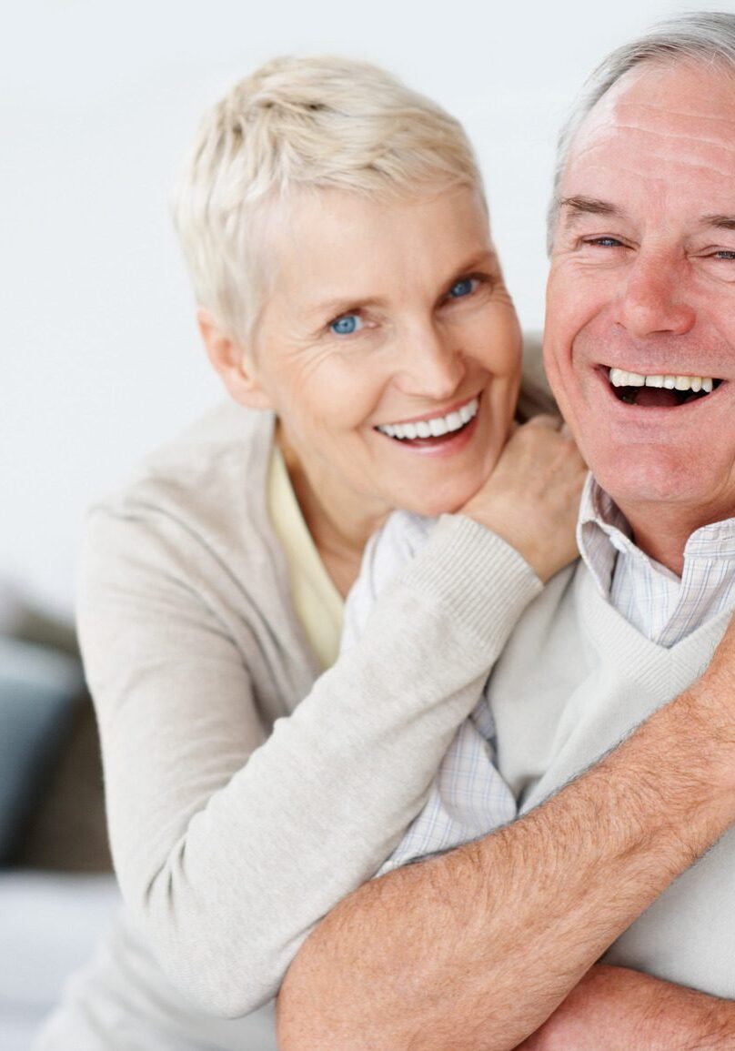 A woman hugging an older man in front of a wall.