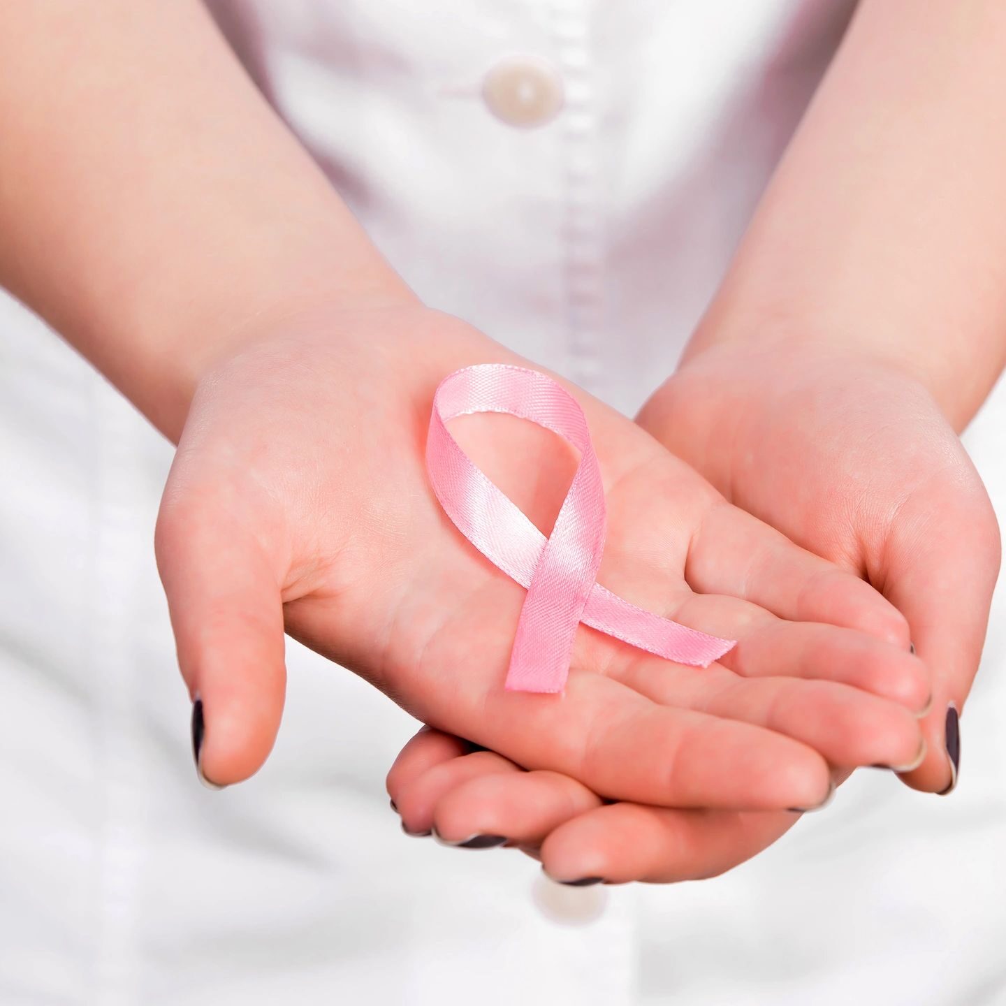 A woman holding her hands with a pink ribbon.