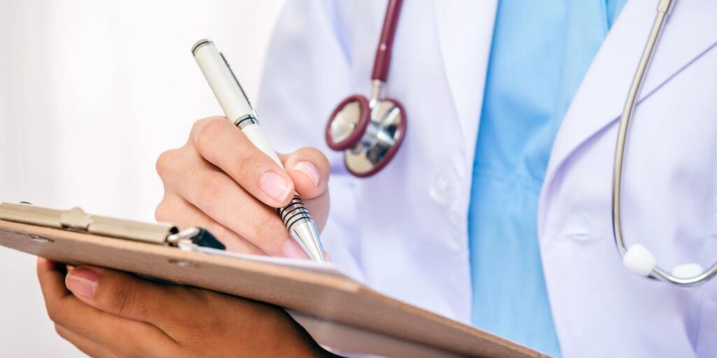 A doctor writing on a clipboard with stethoscope around neck.