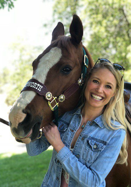 A woman smiles while holding the reins of her horse.